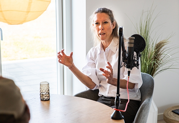 Kvinde siddende ved et bord igang med at optage podcast
