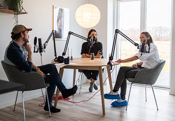 To kvinder og en mand sidder ved bord og optager podcast på flyvestation værløse