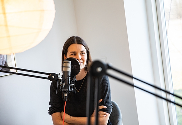 Ung kvinde sidder ved et bord med mikrofoner og optager podcast